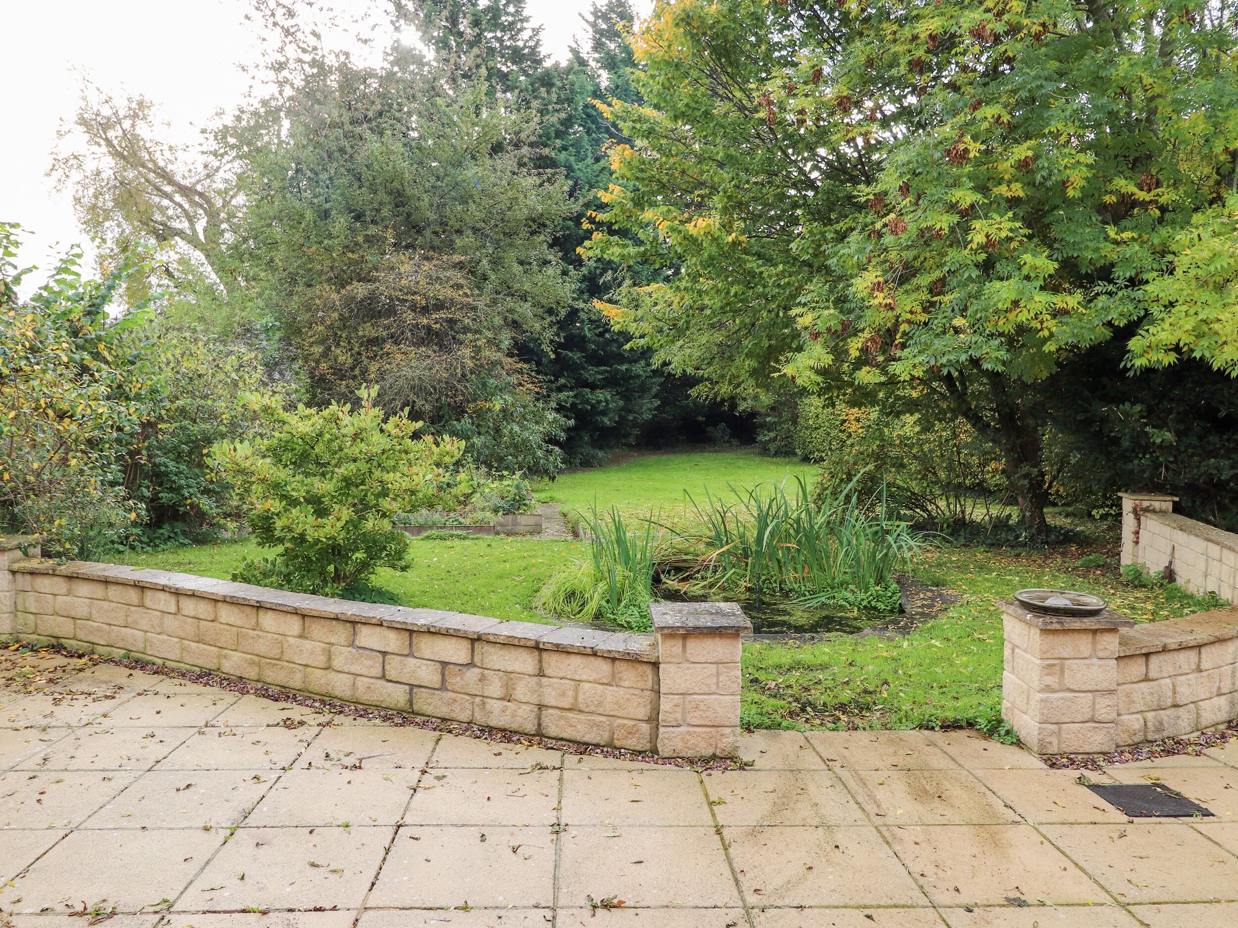 A stone wall with a paved walkway leading to a grassy area with trees and shrubs.
