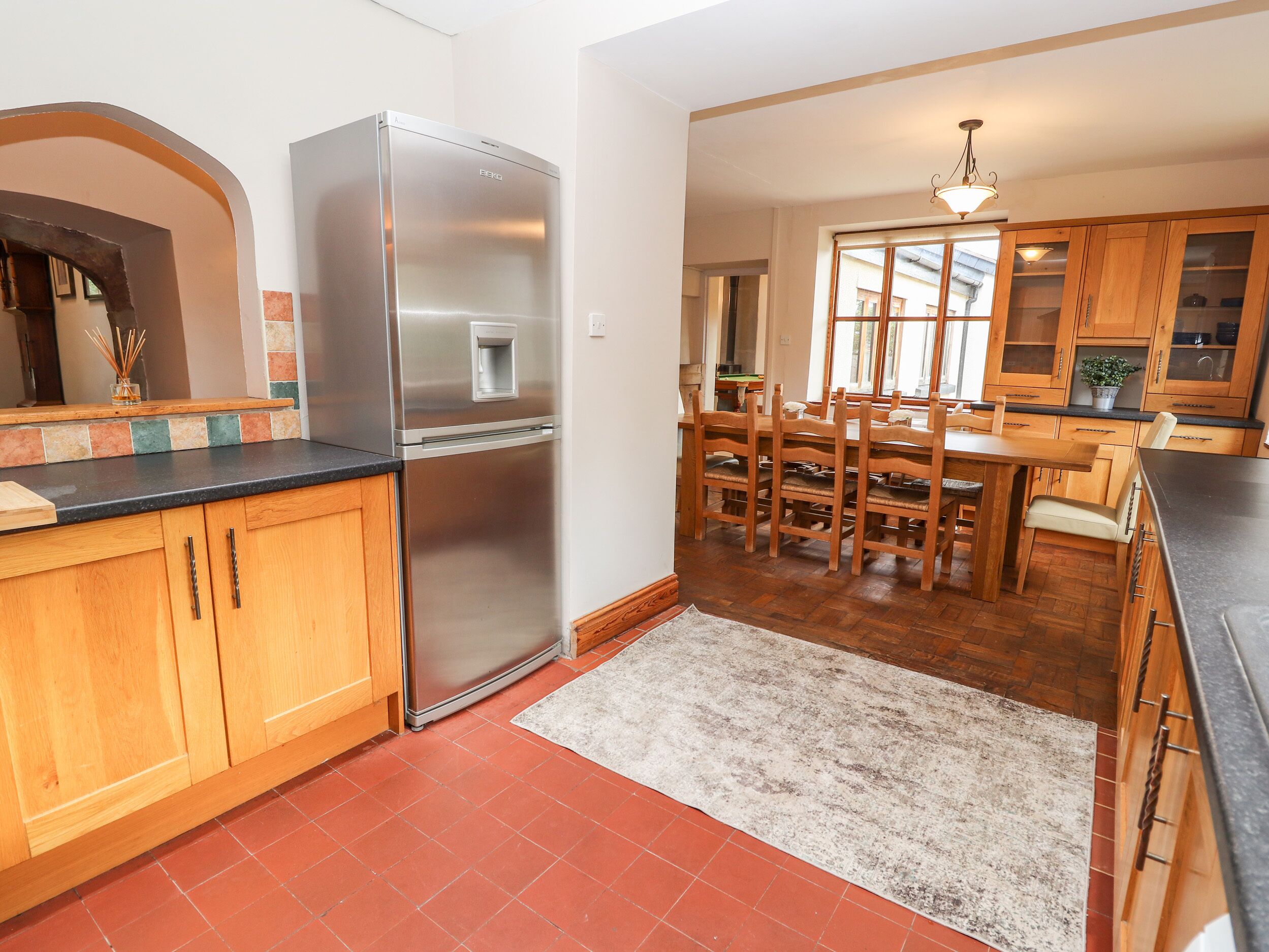 A kitchen with wooden cabinets, a stainless steel refrigerator, a dining table with chairs, and a large window.
