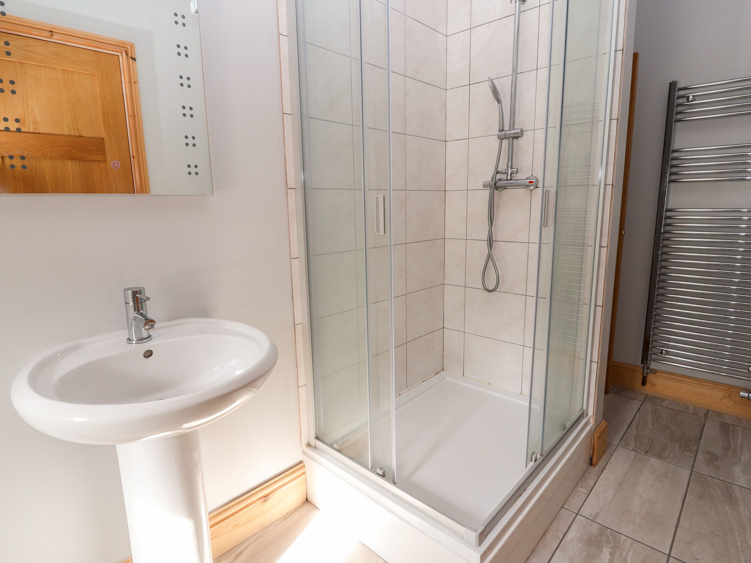 A bathroom with a glass-enclosed shower, a white sink, and a wooden cabinet.
