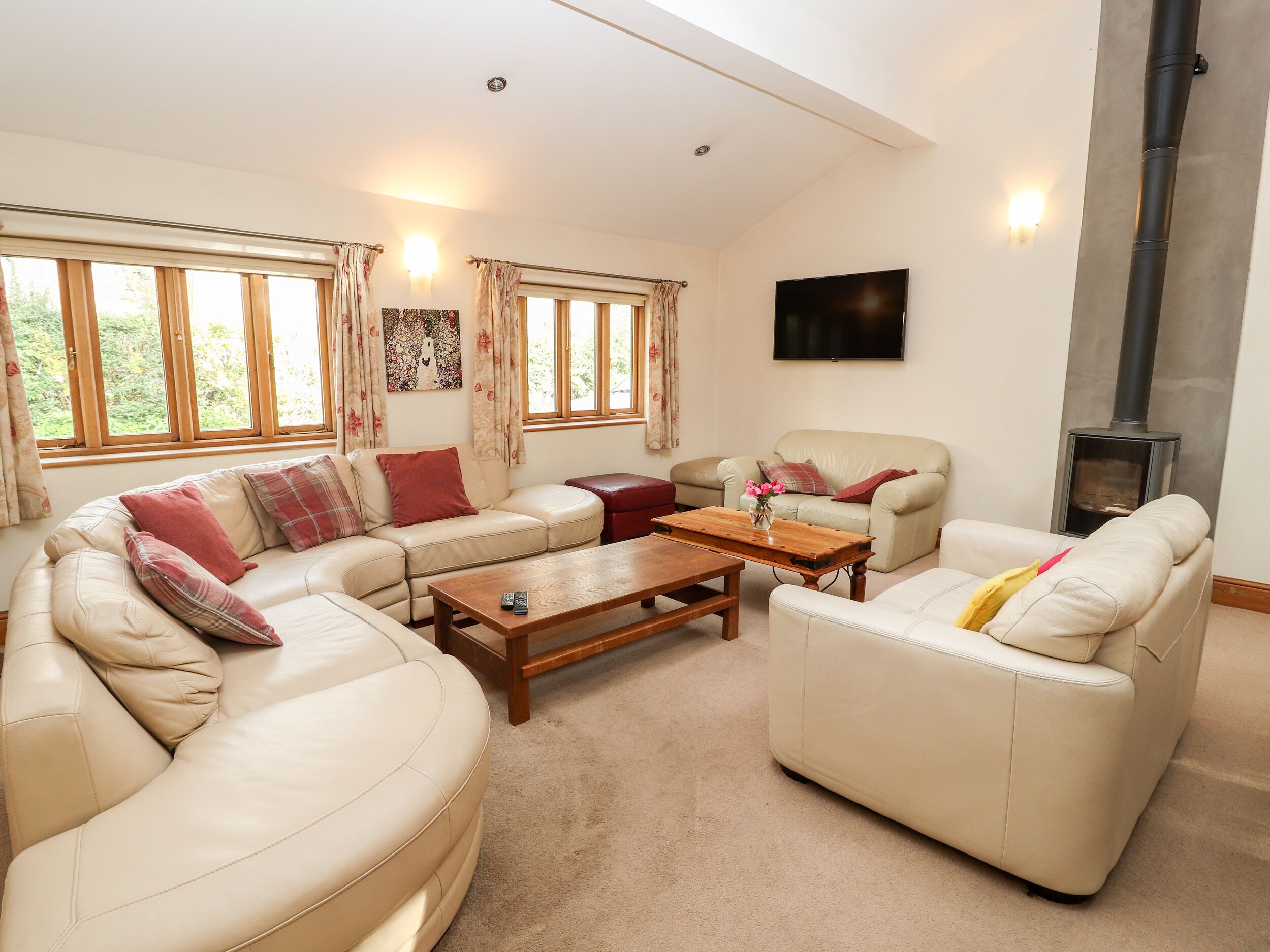 A spacious living room with a high ceiling, a fireplace, and a flat-screen TV mounted on the wall.