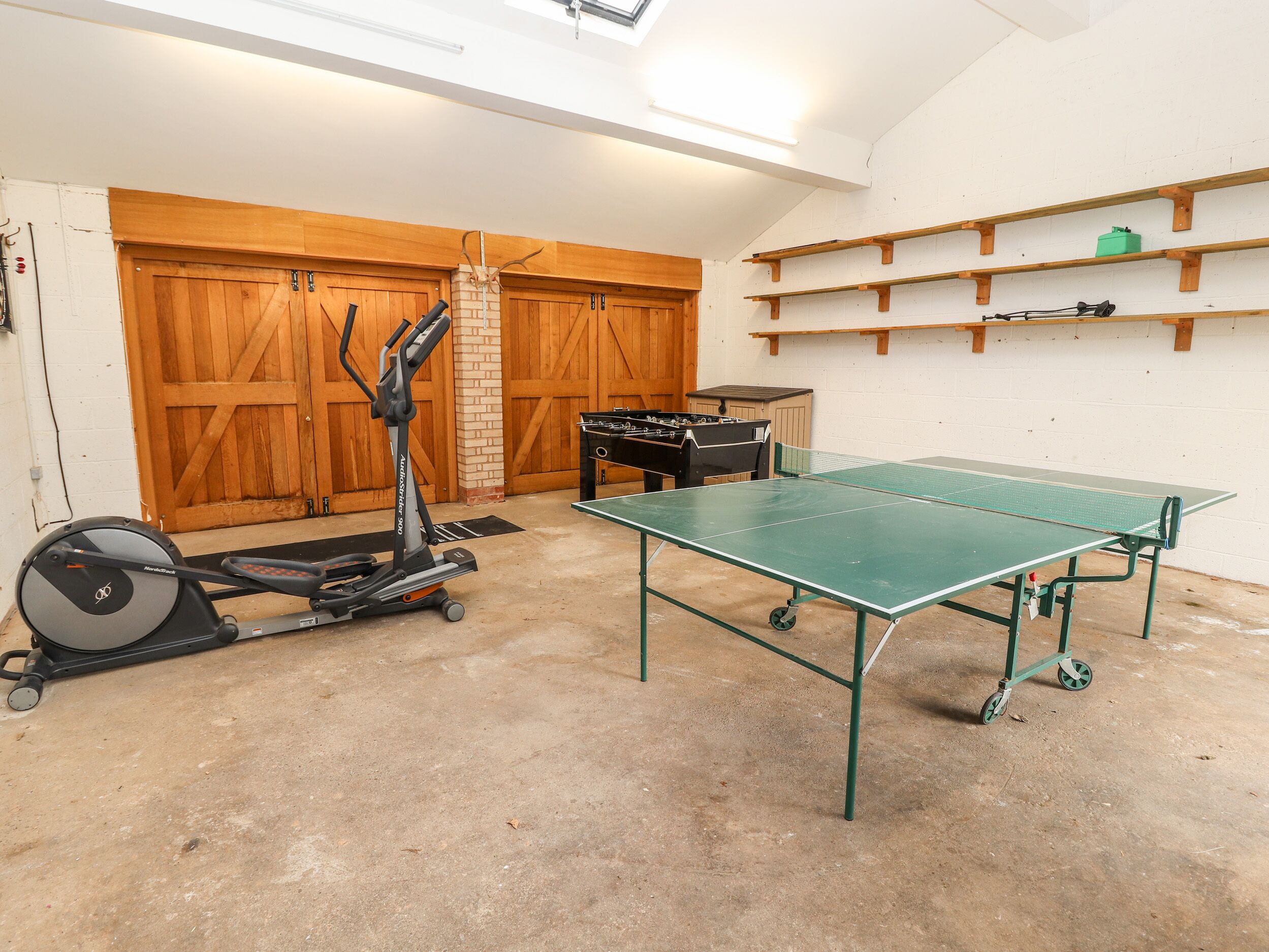 A room with a ping pong table, exercise equipment, and a garage door.