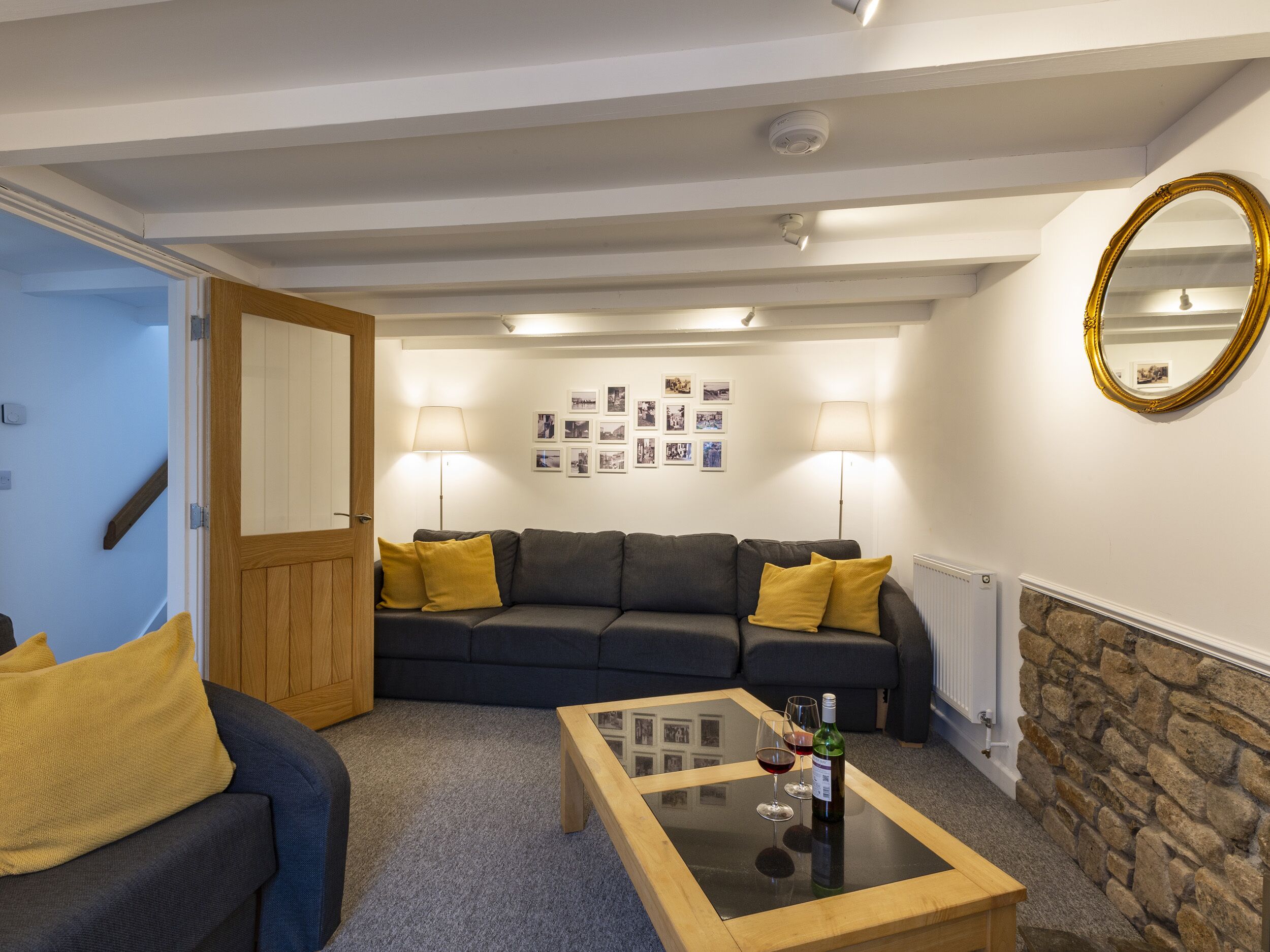 Ein Wohnzimmer mit einem dunkelgrauen Sofa, gelben Kissen, einem Glastisch und einer Steinwand.