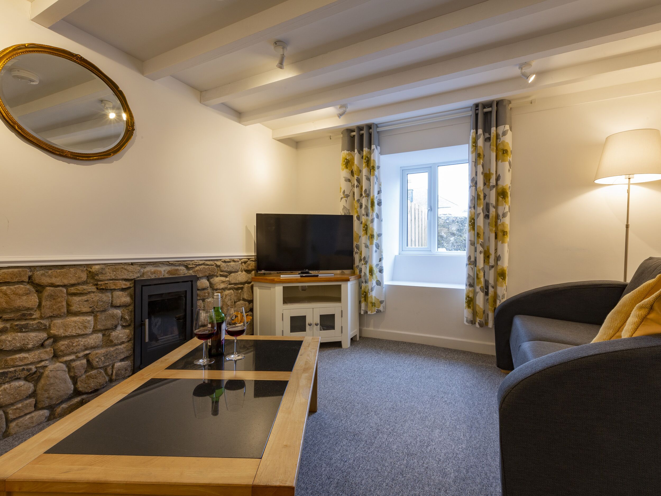 Een woonkamer met een stenen openhaard, een flatscreen televisie, een bank en een tafel met glazen.