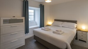 Un dormitorio con cama, mesitas de noche, cómoda, ventana con cortinas e iluminación en el techo.