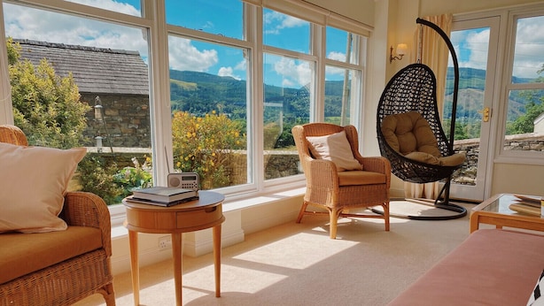 A cozy room with wicker furniture, a hanging chair, and a view of the countryside. - One The Howe (Keswick)