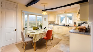 A kitchen with a dining area, featuring a table set for two, a toaster, and a view of the outdoors. - One The Howe (Keswick)