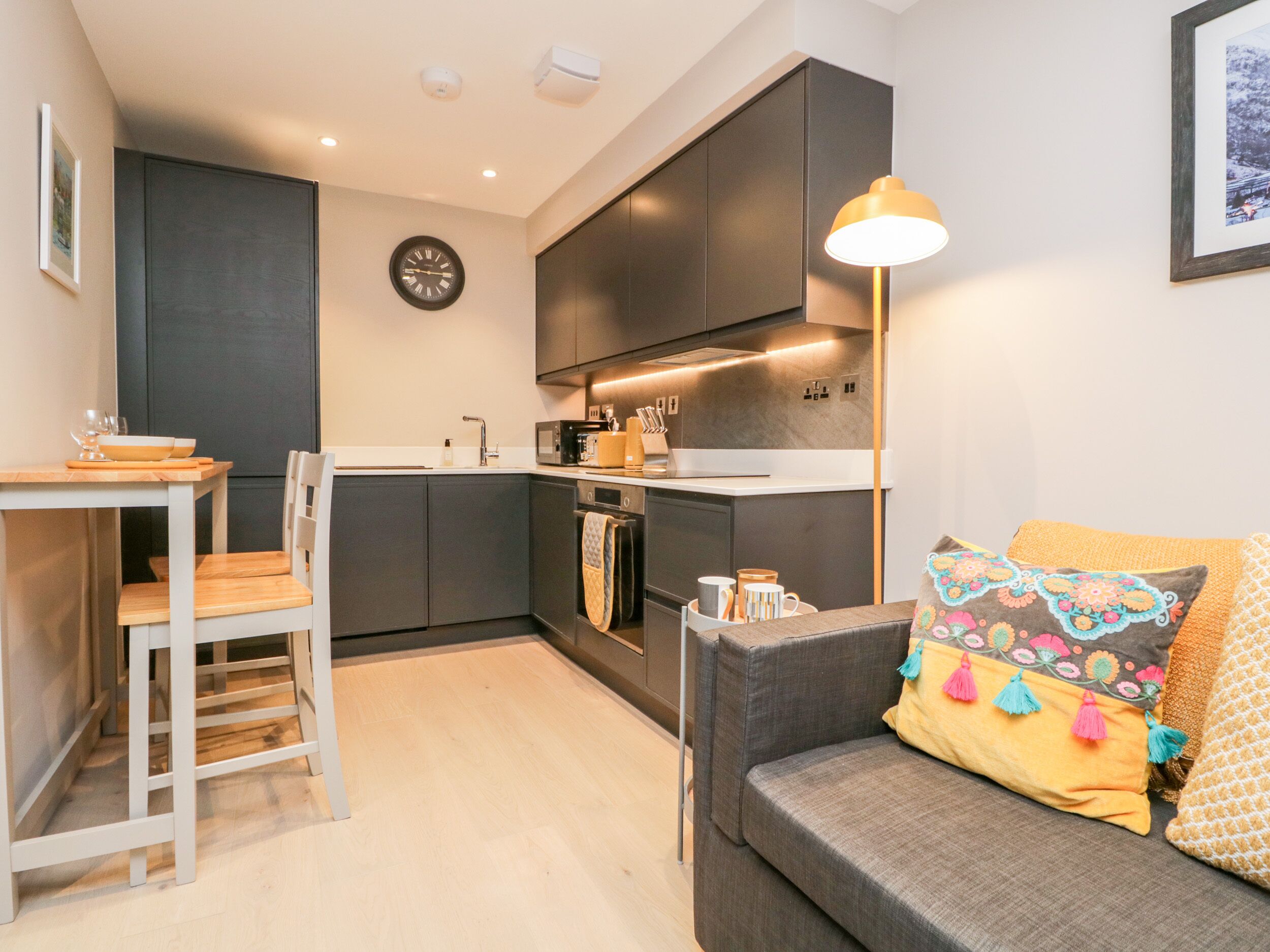 En kompakt opholdsstue med tekøkken, spiseplads og siddeområde med sofa og puder.