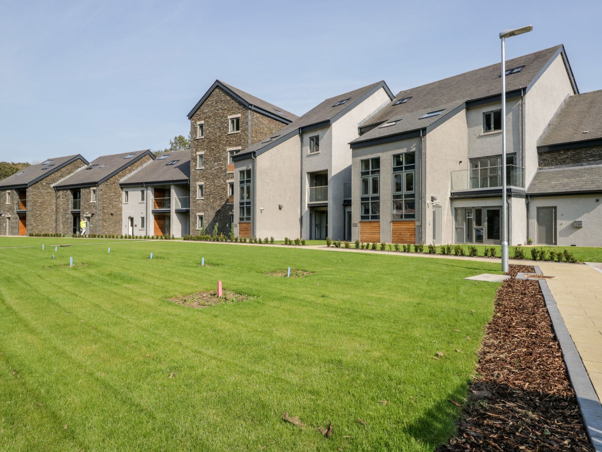 A modern residential building with a flat roof, large windows, and a well-maintained lawn.