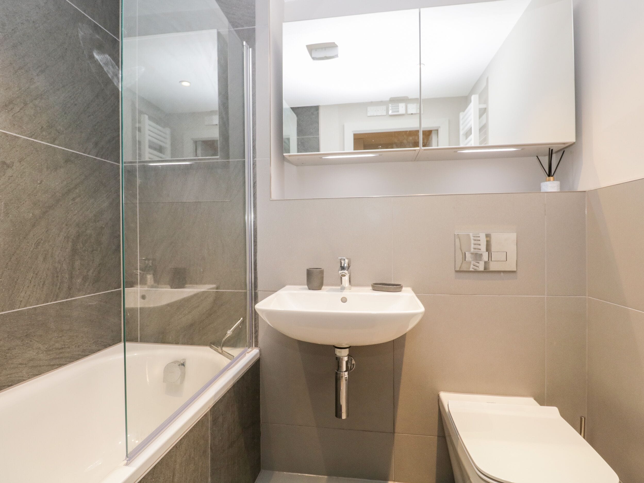 Et moderne badeværelse med brusekabine i glas, vask i hvidt og toilet.