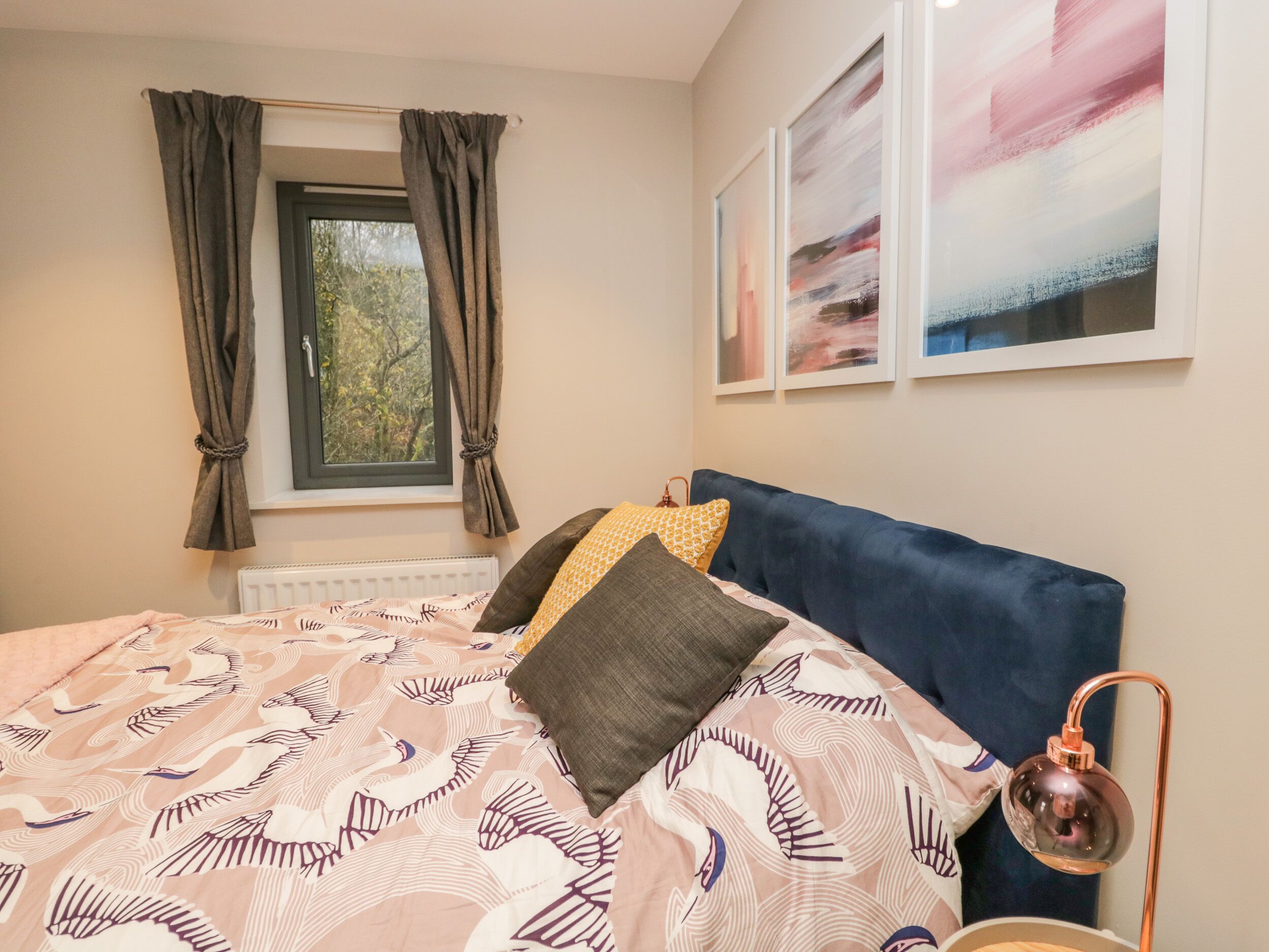 Een slaapkamer met een bed, een raam met gordijnen, een radiator en wanddecoratie.