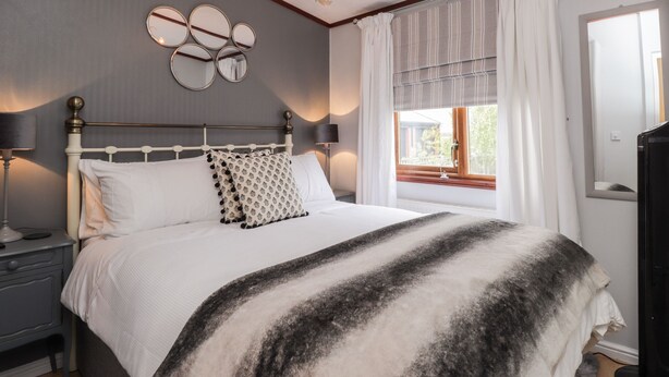A neatly arranged bedroom with a large bed, bedside tables, a chandelier, and a window with curtains.