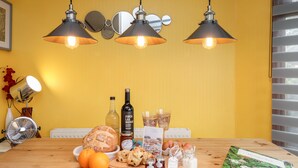 A wooden table with a loaf of bread, oranges, jars of jam, and a bottle of wine.