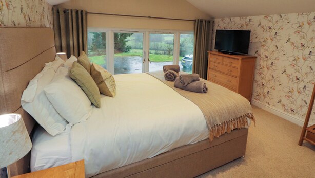 A bedroom with a large bed, a television, and a view of the outdoors. - Cragfell Cottage (Windermere)