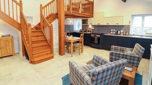 A modern kitchen with a built-in microwave, a dining area with a wooden table and chairs, and a staircase leading to an upper level. - Cragfell Cottage (Windermere)