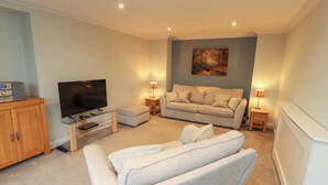 A living room with a sofa, television, and a painting on the wall. - Cragfell Cottage (Windermere)