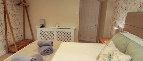A bedroom with a bed, a wooden hanger, a desk with a lamp, and a door.