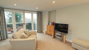 A living room with a sofa, ottoman, TV, and a cabinet. - Cragfell Cottage (Windermere)