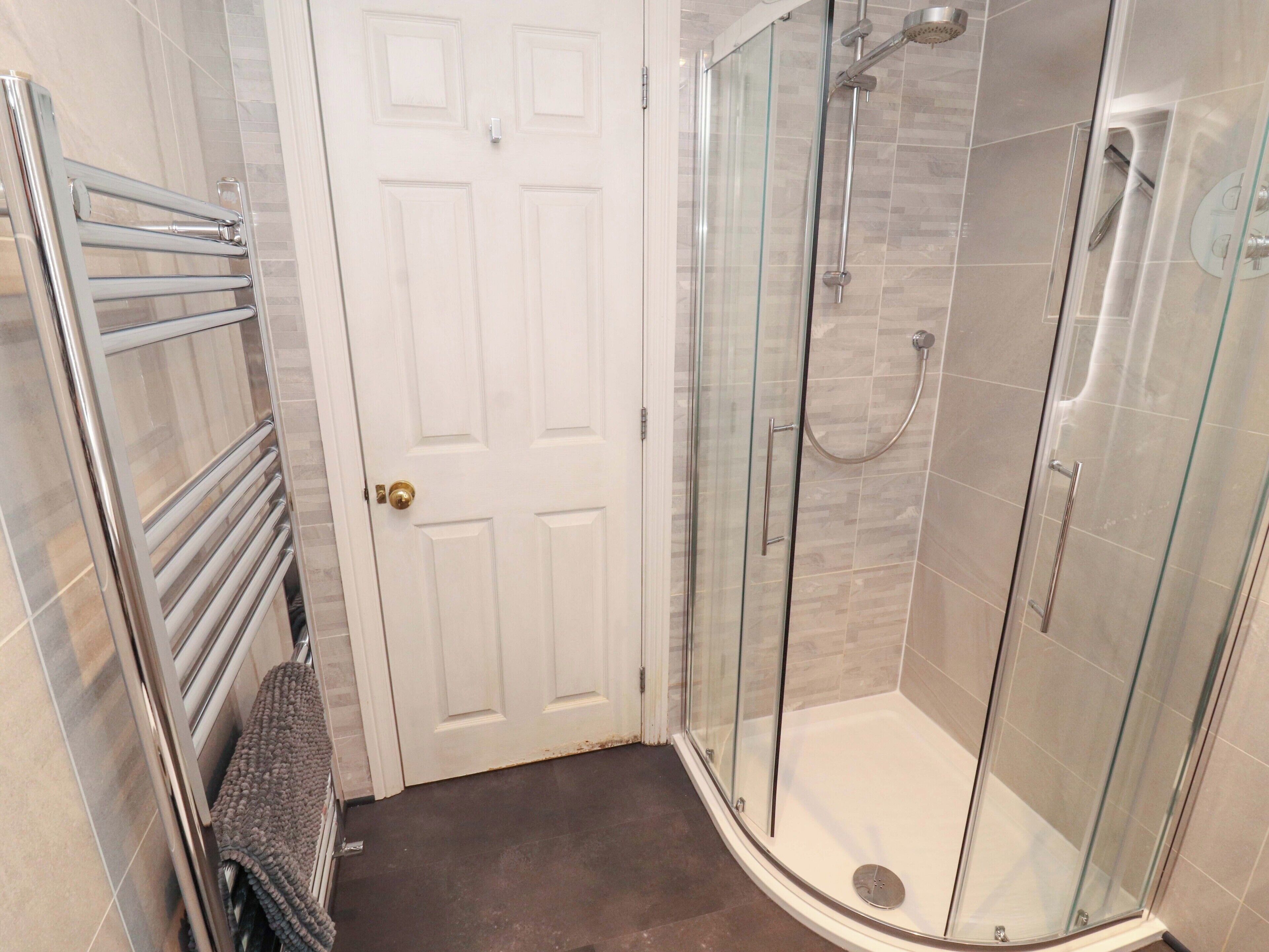 A modern bathroom with a glass shower enclosure, a towel rack, and a door.