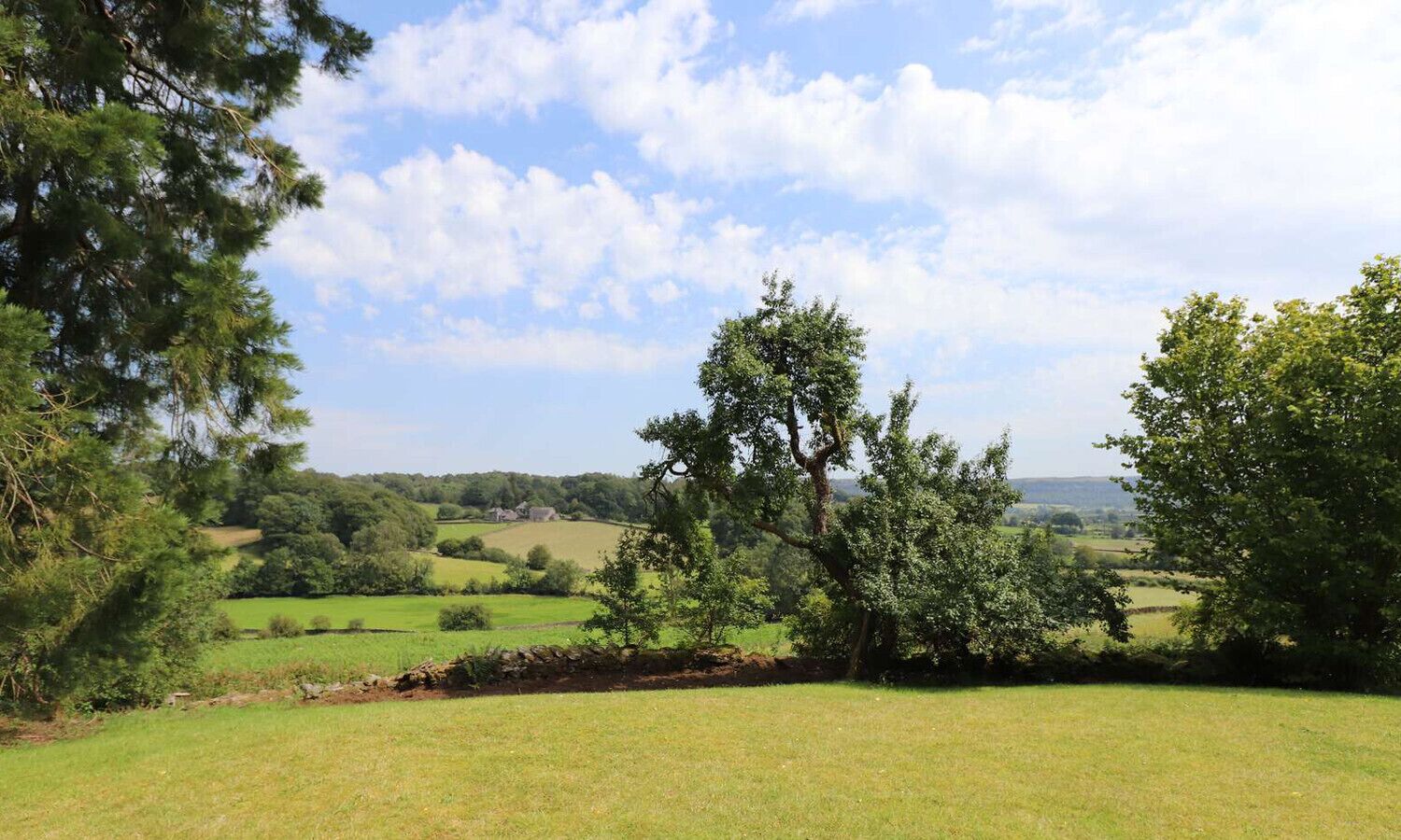Un paysage rural avec un mur de pierres, des champs couverts d’herbe et des arbres.