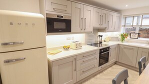 Une cuisine moderne équipée d’un four encastré, d’un micro-ondes et d’un grille-pain. On y trouve une table à manger avec des chaises, ainsi qu’une fenêtre avec des stores.