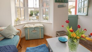 A cozy room with a bay window, a small chest of drawers, a blue sofa, and a vase of tulips. - 2 Linden Terrace (Sandown)