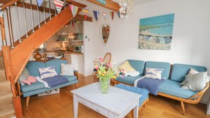 A cozy living room with a wooden staircase, blue sofas, a white coffee table, and a painting of a coastal scene. - 2 Linden Terrace (Sandown)