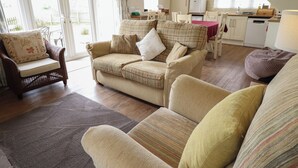 A cozy living room with a sofa, armchair, and ottoman, a dining area with a table and chairs, and a kitchen with a refrigerator and cabinets. - Shepherd's Cottage (Alford)