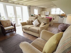 A cozy living room with a sofa, armchair, and a dining area with a table and chairs. - Shepherd's Cottage (Alford)