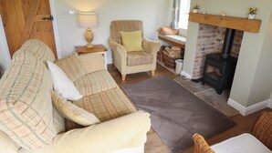 A cozy living room with a fireplace, a sofa, a chair, and a lamp. - Shepherd's Cottage (Alford)