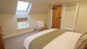 A bedroom with a skylight, a bed with a green blanket, a wooden door, and a window with a view of a white fence. - Shepherd's Cottage (Alford)