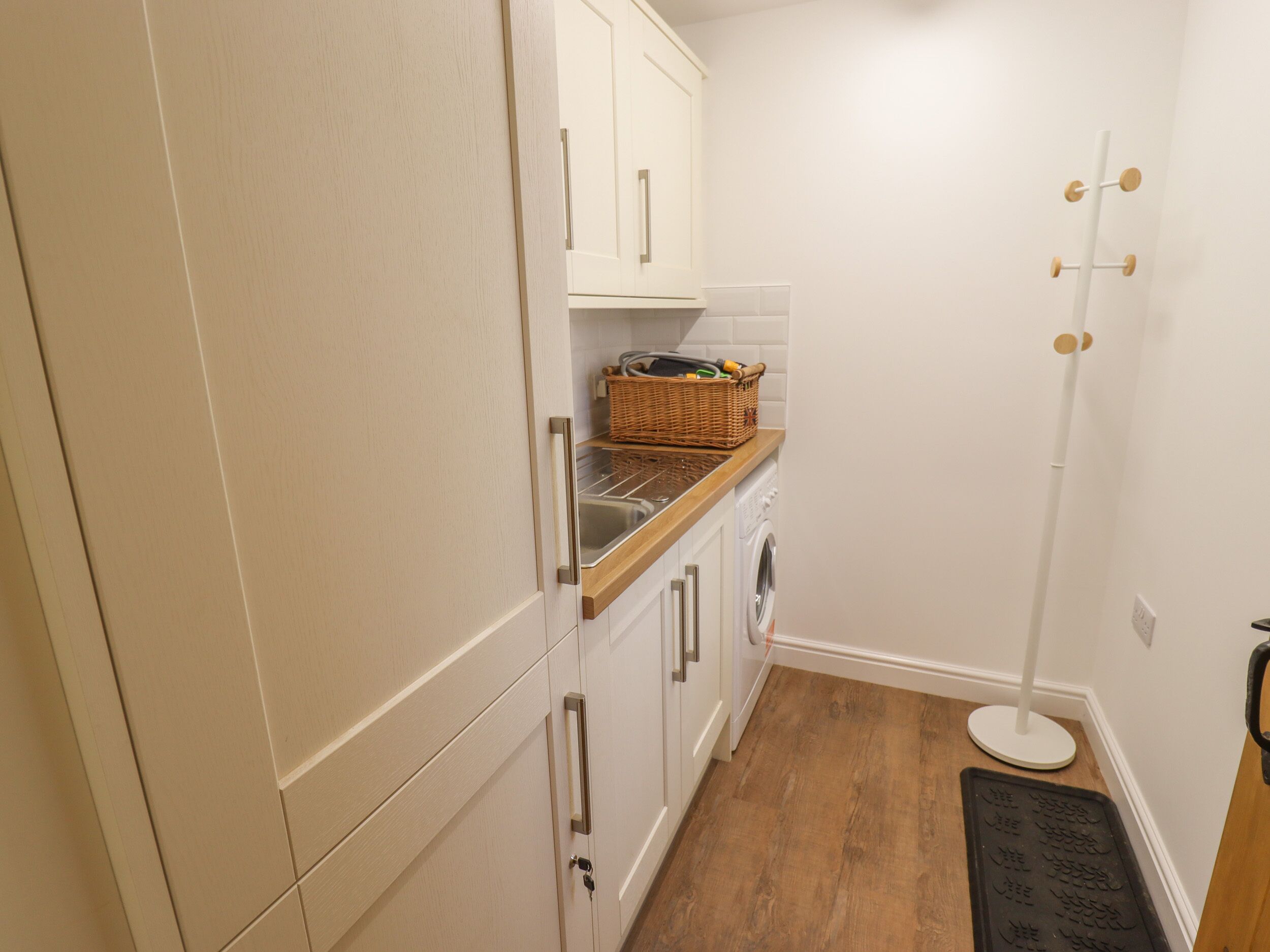 Cocina compacta con armarios blancos, encimera de madera, lavadora y una cesta de mimbre en la encimera.