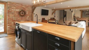 A modern kitchen with a wooden countertop, black cabinets, and a built-in washing machine. - The Courtyard - Hilltop Barn (Blandford Forum)