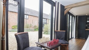 A modern interior with large windows, a wooden table with chess pieces, and two upholstered chairs. - The Courtyard - Hilltop Barn (Blandford Forum)