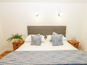 A neatly made bed with striped pillows and a patterned bedspread, two bedside tables with decorative items, and wall-mounted lights. - Macaw Cottages No 4 (Kirkby Stephen)