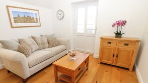 A living room with a beige sofa, a wooden coffee table, a wooden cabinet, and a clock on the wall. - Macaw Cottages No 4 (Kirkby Stephen)