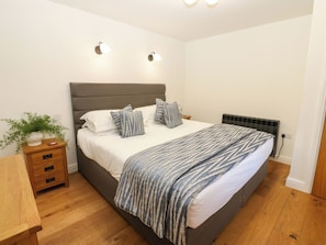 A bedroom with a bed, bedside tables, a radiator, and wall-mounted lights. - Macaw Cottages No 4 (Kirkby Stephen)