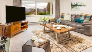 Un salon moderne doté d’un téléviseur à écran plat, d’un meuble de rangement en bois, d’un canapé en cuir et d’une grande fenêtre offrant une vue panoramique.