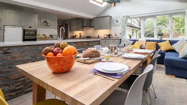 Une cuisine moderne dotée d’un grand îlot central, un coin repas avec une table en bois et un salon avec un canapé bleu.