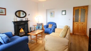 A living room with a fireplace, two sofas, a coffee table, and a wooden door. - Ard an Phíobaire (Bunbeg)