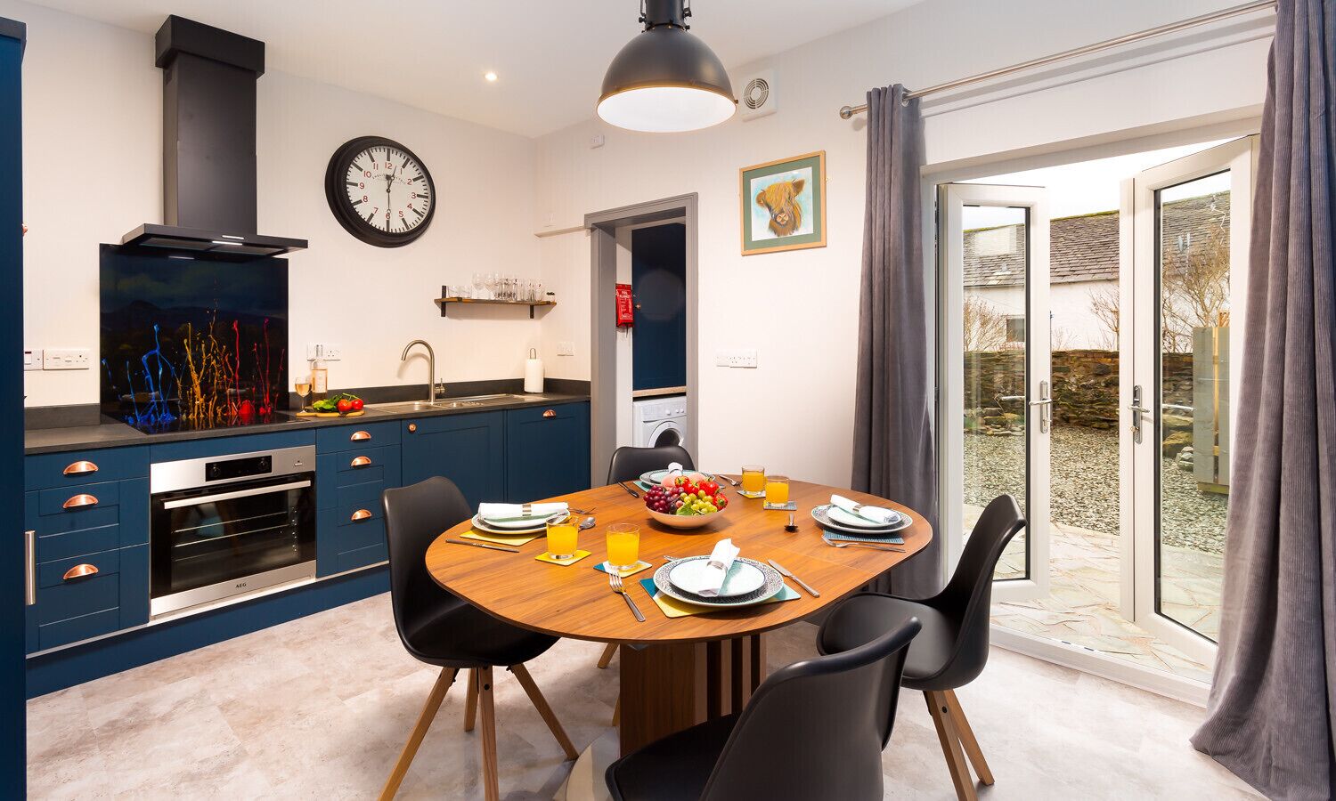 Una cucina moderna con mobili blu, forno integrato e zona pranzo con tavolo e sedie in legno.