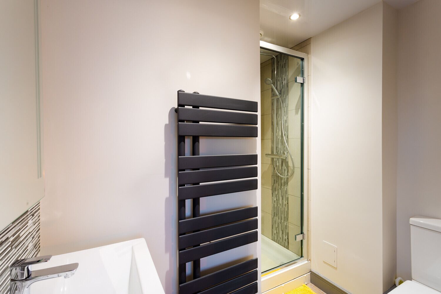 A modern bathroom with a glass shower enclosure, a black towel rack, and a white sink.