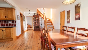 A spacious dining area with a wooden table and chairs, a staircase, and wooden cabinets. - Crolly Home (Crolly)