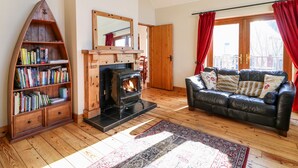 A cozy living room with a fireplace, a bookshelf, a leather sofa, and a large window with curtains. - Crolly Home (Crolly)