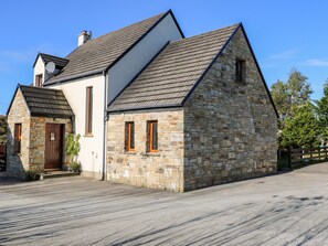 A stone building with a gabled roof, a wooden door, and a small porch with potted plants. - Crolly Home (Crolly)