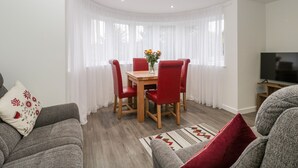 A modern living room with a dining area, featuring a wooden table and red chairs, a grey sofa, and a TV in the corner. - Flat 2, 38 Preston Road (Weymouth)