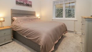A bedroom with a bed, bedside tables, a dresser, a window with a view of rocks, and a painting on the wall. - Flat 2, 38 Preston Road (Weymouth)