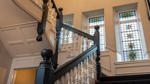 Un magnifique escalier, orné de balustres travaillés et doté d’une rampe sombre, menant à un palier agrémenté d’un vitrail.