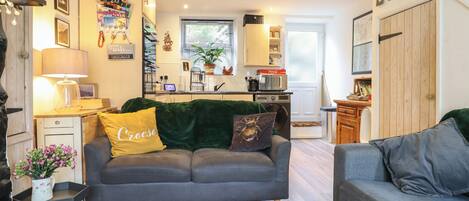 Een gezellige woonkamer met een grijze bank, een kleine tafel met een lamp en een houten bankje.