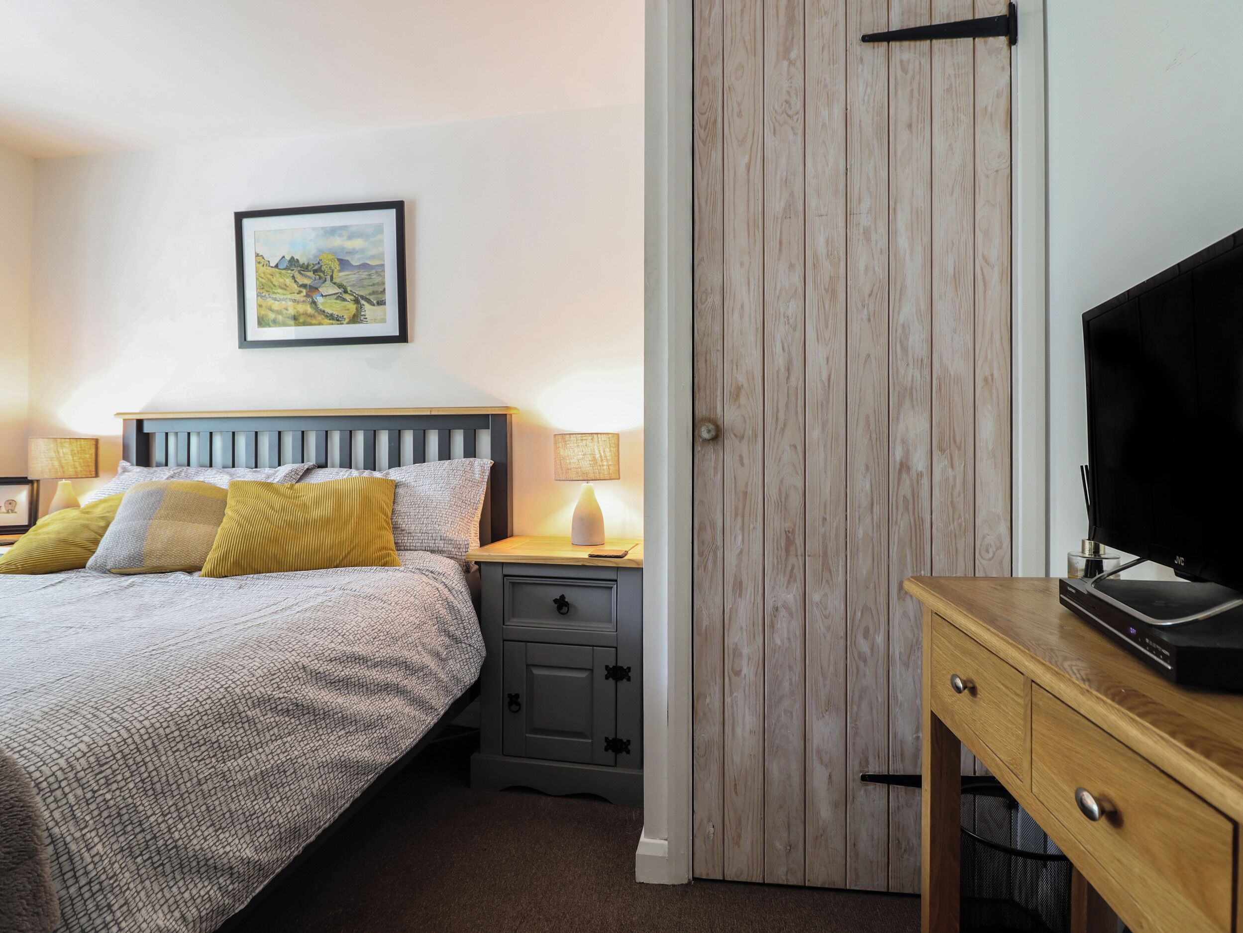 A neatly arranged bedroom with a bed, bedside lamps, a wooden wardrobe, and a TV stand.