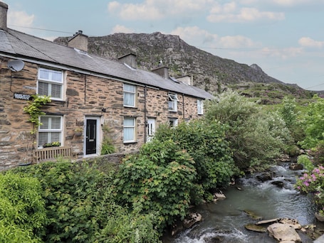 A stone building with a sign reading "Barlwyd Terrace," a small stream, and a mountainous backdrop.